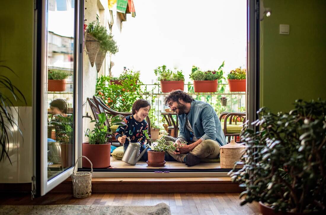 Plantas seguras para hogares con niños Padre e hijo sonriendo, sentados en el piso, regando plantas con una regadora.