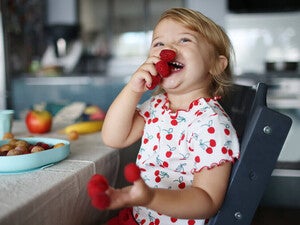 Niña pequeña en la cocina comiendo frambuesas feliz
