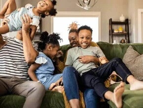 Familia, papá, mamá e hijos en el sofá sonriendo, resultado de crianza consciente y respetuosa