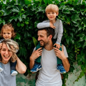 Mamá y papá al aire libre, alzando cada uno a sus hijos sobre sus hombros y sonriendo.