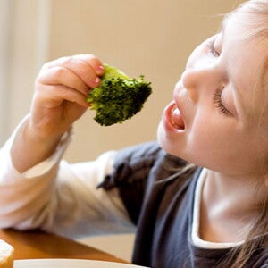 Una niña alimentándose con un brócoli.  