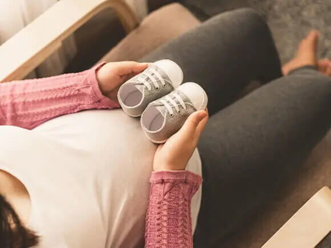 Descubre cómo brindar amor y cuidado al bebe Una mujer embarazada sosteniendo calzados de bebe