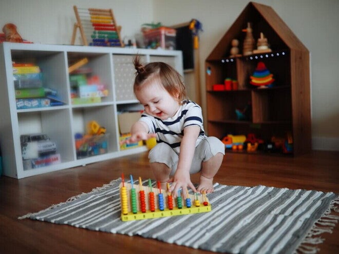 Niña de dos años jugando sobre la alfombra con ábaco de madera. Juego tranquilo como rutina diaria.