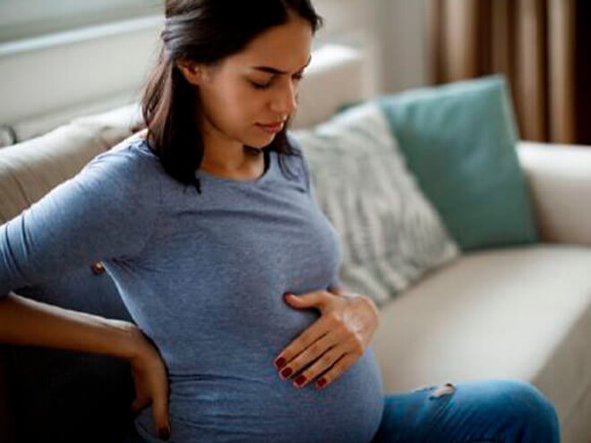 Conoce qué es la eclampsia y cuáles son sus causas. Mamá tocando el vientre y la espalda sintiendo molestia.