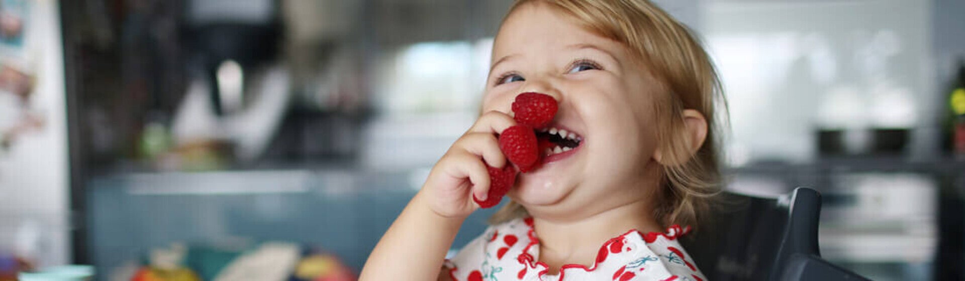 Niña pequeña en la cocina comiendo frambuesas feliz