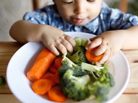 Nutrientes que fortalecen las defensas niño comiendo plato de verduras