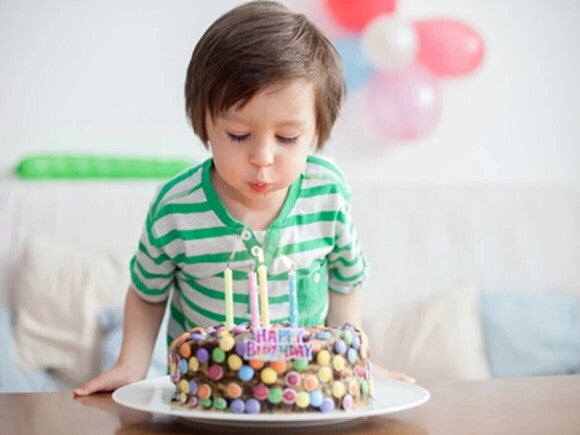 Niño pequeño soplando las velas de un pastel de cumpleaños en una sala decorada con globos