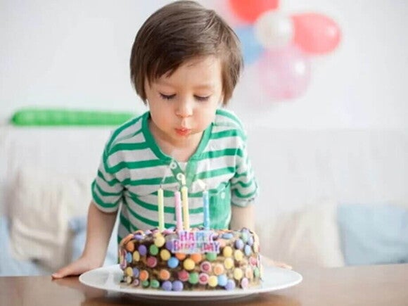 Niño pequeño soplando las velas de un pastel de cumpleaños en una sala decorada con globos.