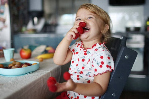 Niña pequeña en la cocina comiendo frambuesas feliz